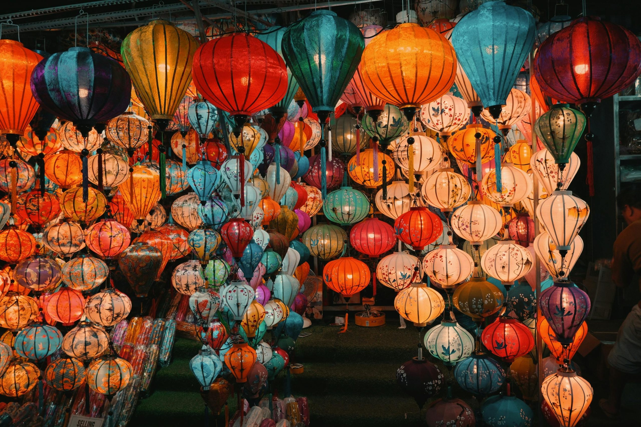 A bustling street in Hoi An Ancient Town at dusk, illuminated by hundreds of colorful silk lanterns hanging overhead, with ancient yellow buildings lining the street and people strolling below.