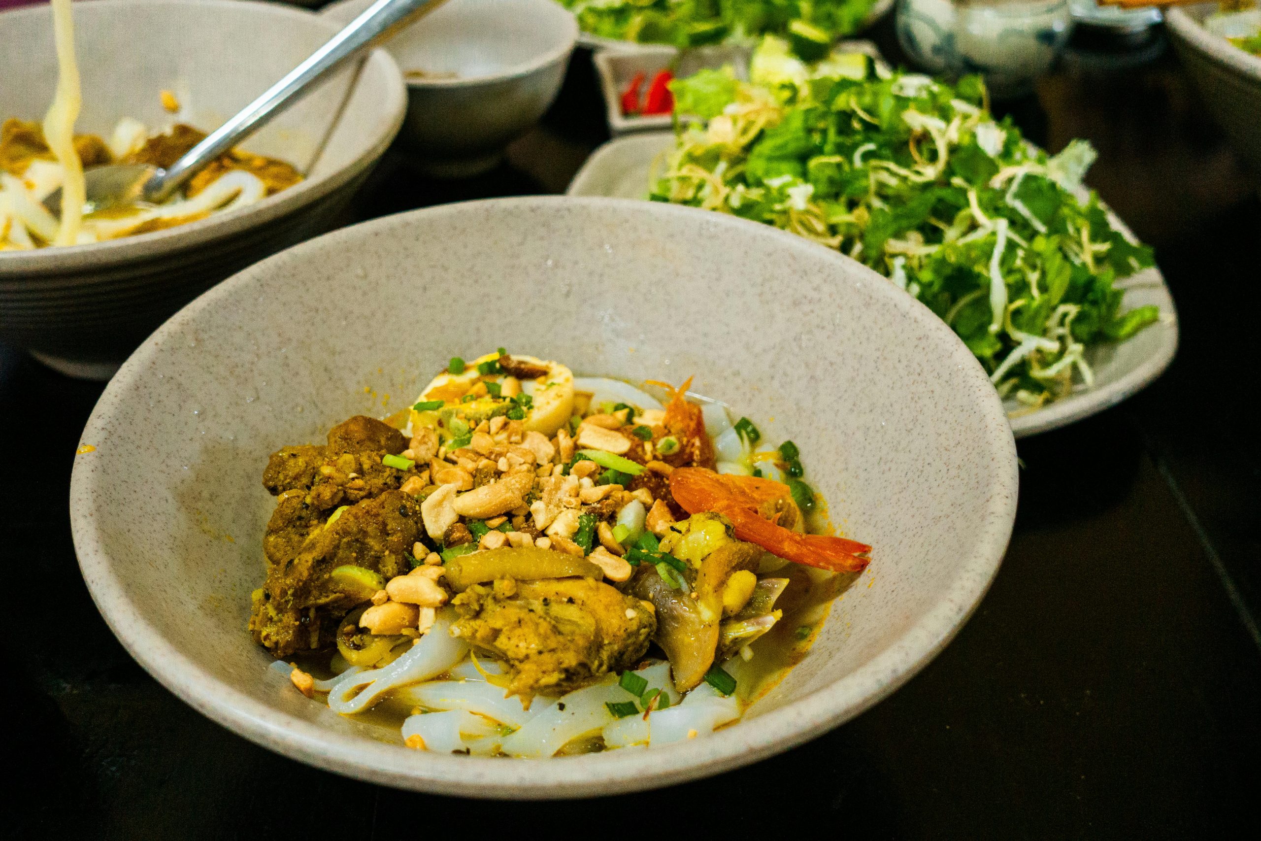 A delicious bowl of Mi Quang, a traditional Vietnamese noodle dish from Da Nang, with yellow noodles, shrimp, pork, fresh herbs, and a quail egg, served with a lime wedge