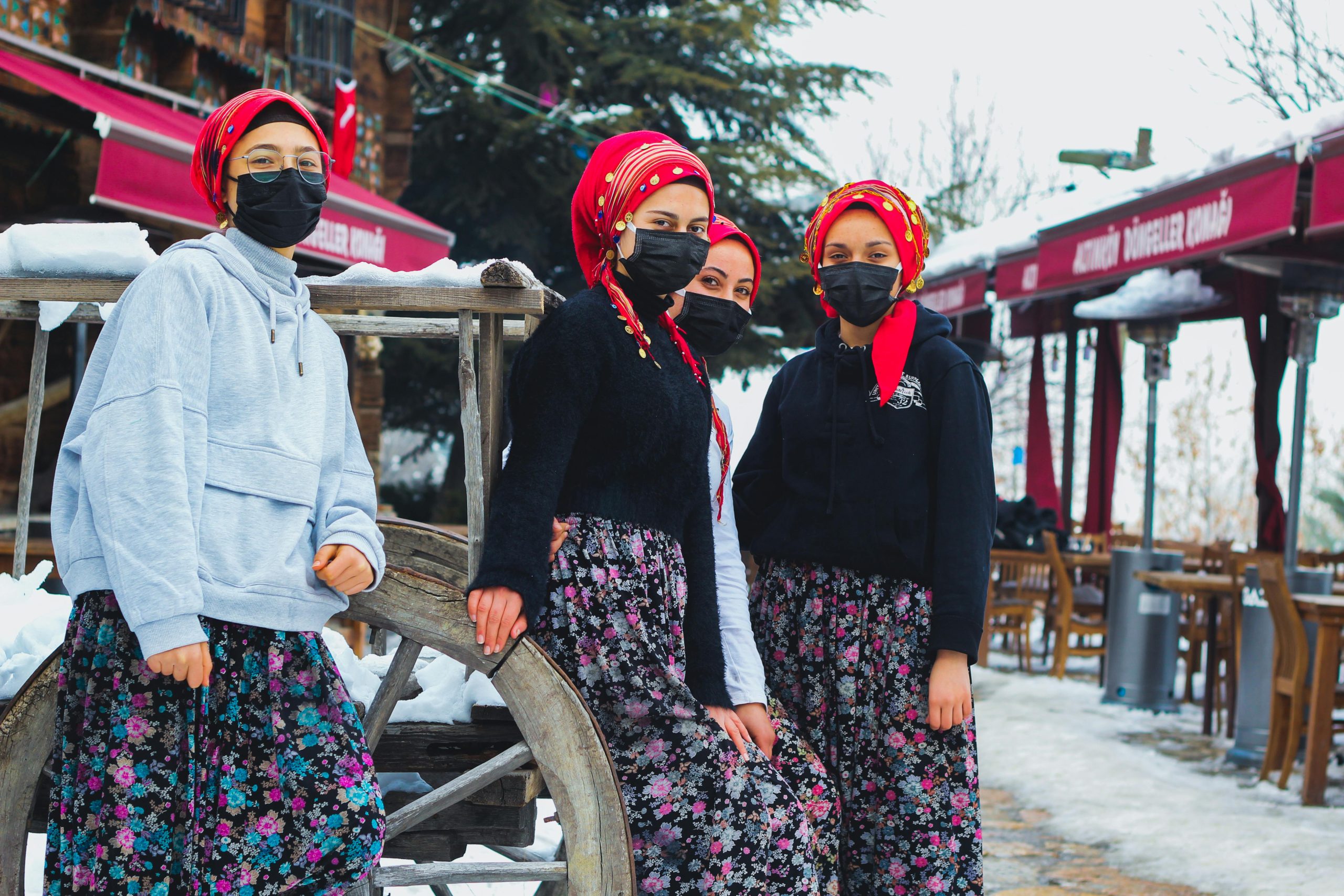 A group of Red Dao women in traditional colorful attire with intricate headscarves smiling and talking in a Sapa village setting.