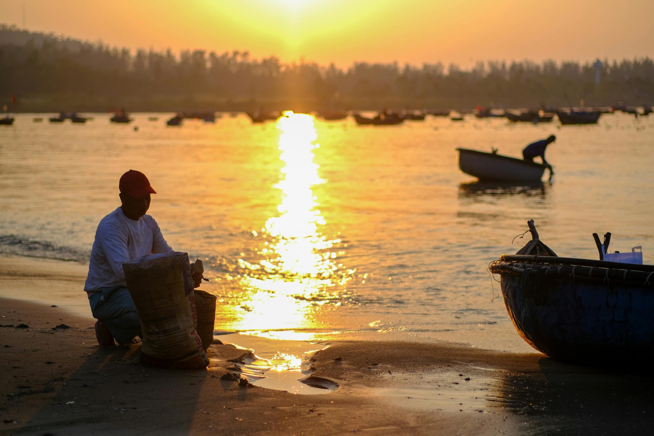 A stunning sunset over My Khe Beach, with vibrant orange, pink, and purple hues reflecting on the calm ocean surface. Silhouettes of palm trees and a few distant fishing boats are visible against the dramatic sky, creating a peaceful and romantic atmosphere.