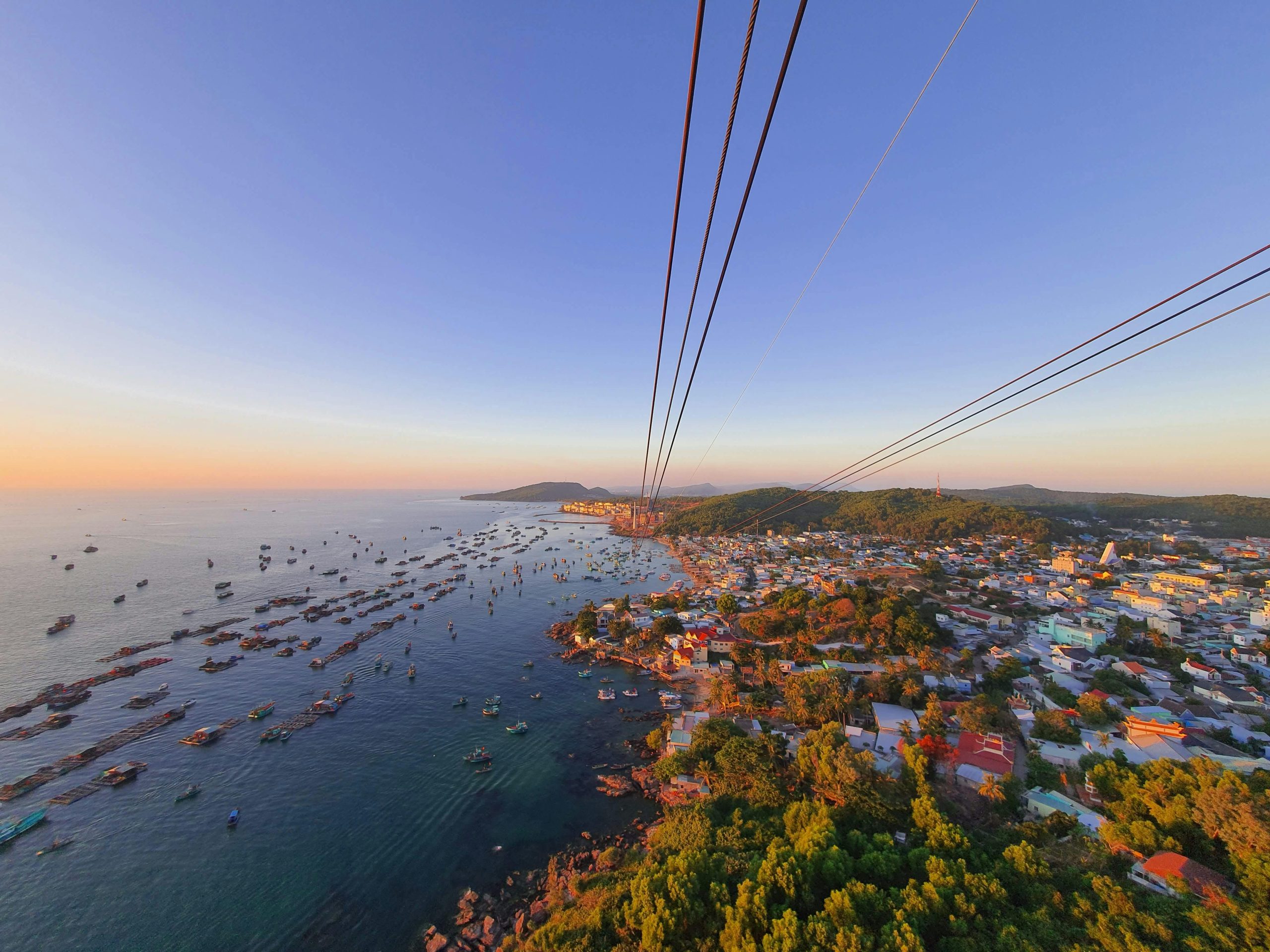 A vibrant aerial view from the Hon Thom Cable Car in Phu Quoc, Vietnam, showcasing numerous small green islands, sparkling blue sea, and the long cable stretching into the distance.