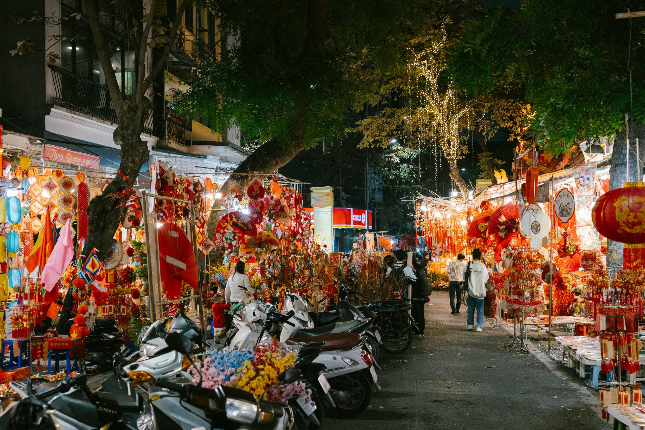 A vibrant night market scene in Hanoi's Old Quarter with colorful lanterns, bustling crowds, and various street food stalls