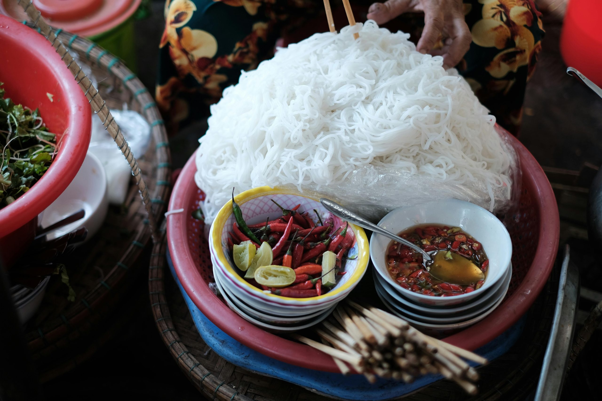A vibrant Vietnamese street food stall in Hanoi selling Bún Chả, with grilled pork, fresh herbs, and noodles visible, and locals enjoying their meal on small plastic stools