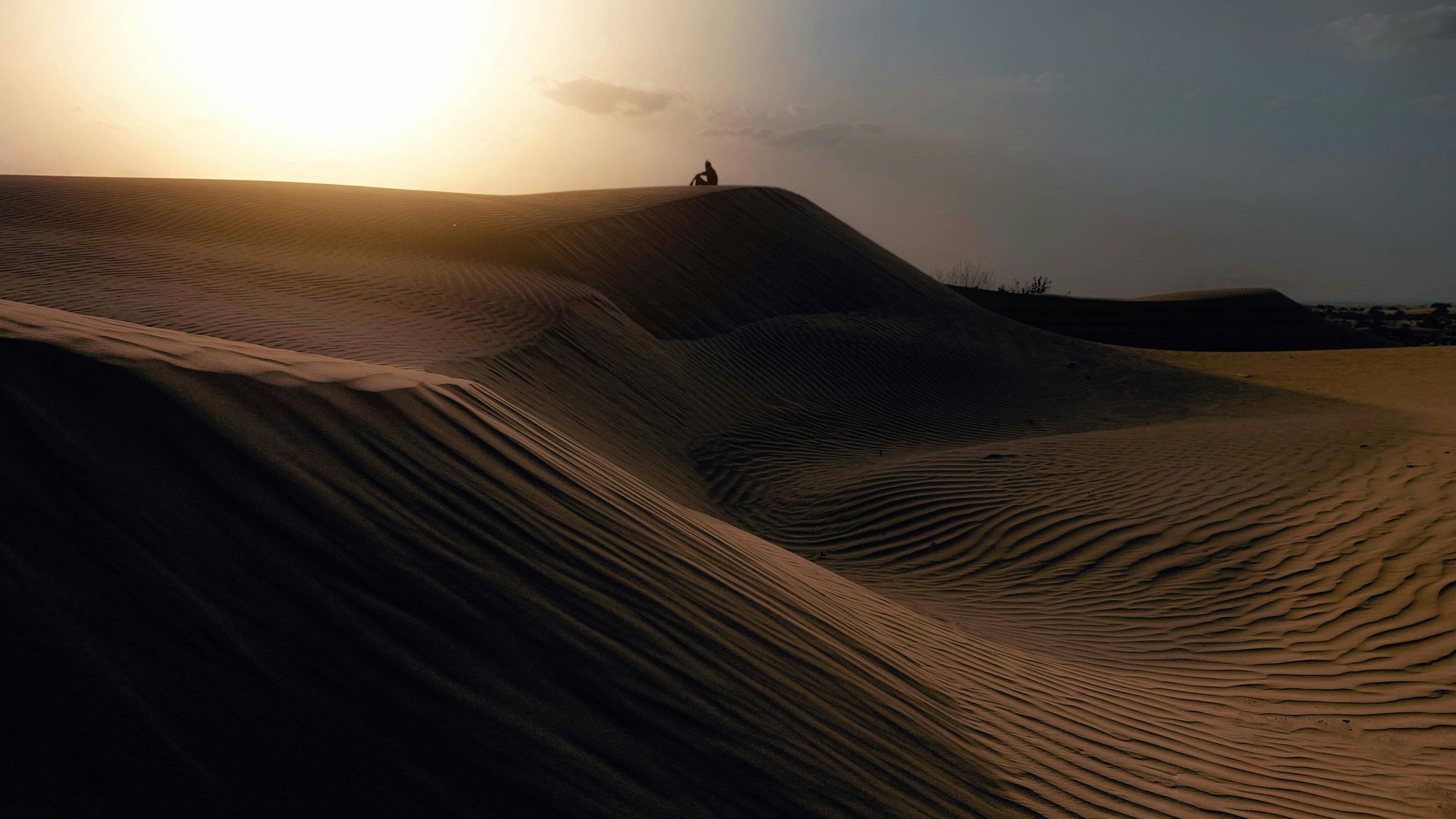 A wide shot of the Red Sand Dunes in Mui Ne at sunset, with golden light illuminating the ripples in the sand and a few tourists silhouetted against the sky, some sandboarding.