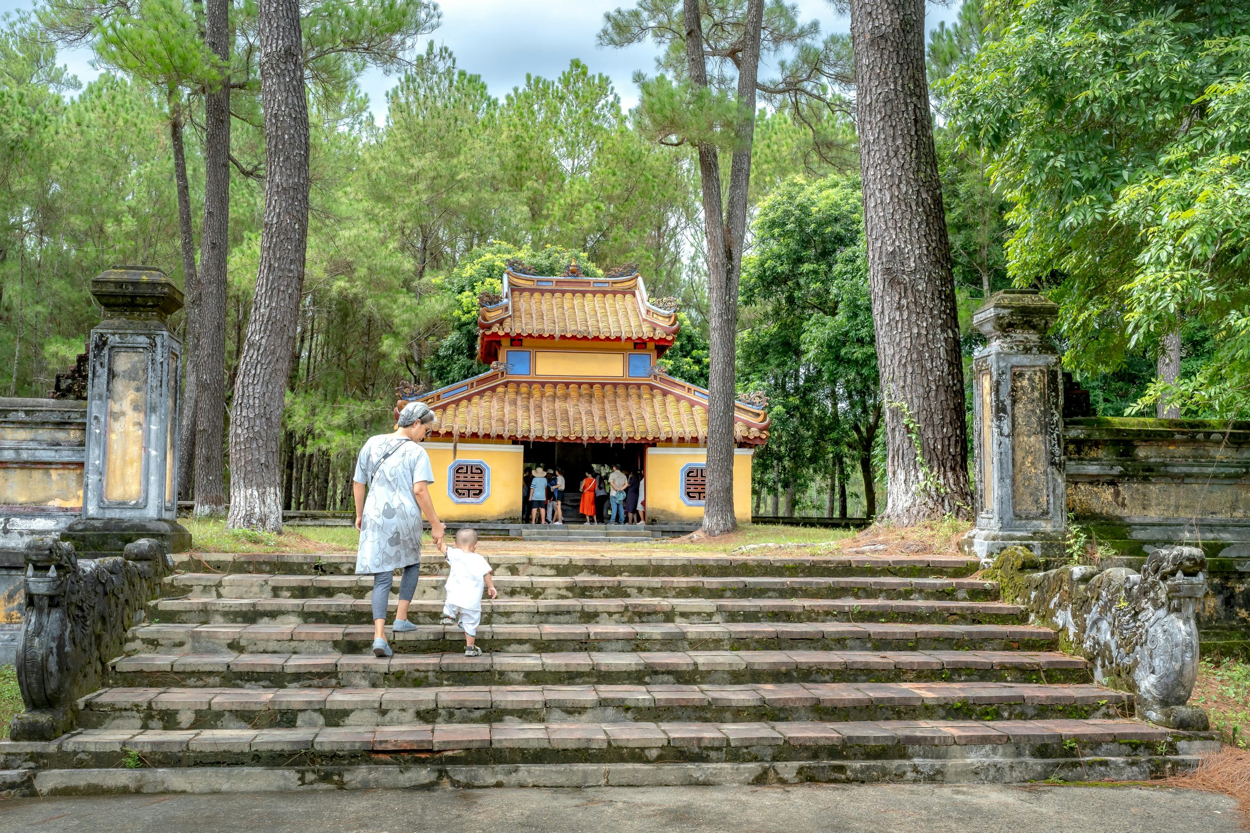 An ancient pagoda, Hoa Yen Pagoda, nestled amidst dense green foliage on Yen Tu Mountain, with stone steps leading up to its entrance. The air is slightly misty, suggesting a sacred and tranquil atmosphere.