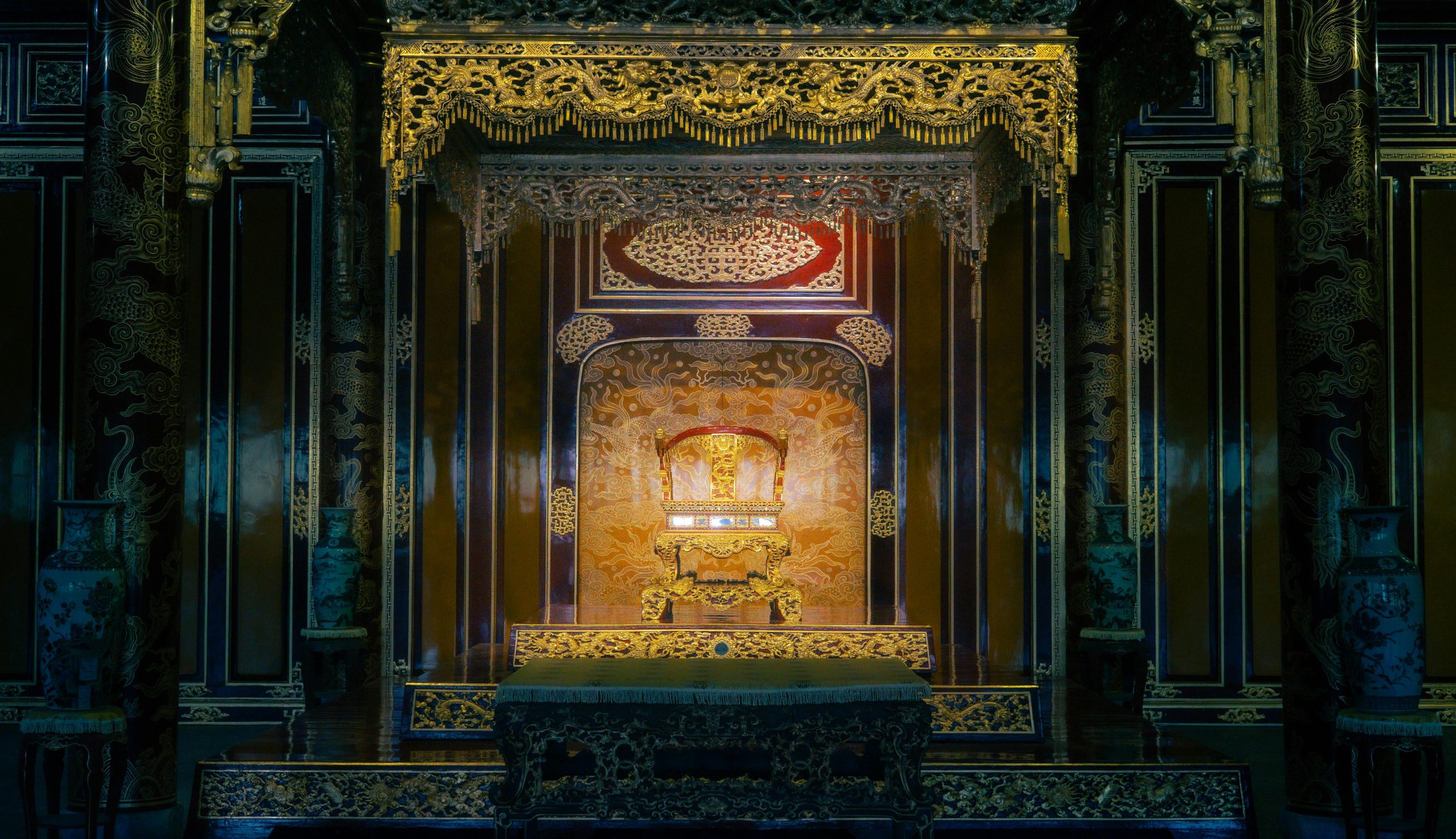An interior shot of the Thai Hoa Palace within the Hue Imperial City, showcasing its ornate golden throne, richly decorated pillars, and traditional Vietnamese architectural details. The lighting is soft, highlighting the grandeur of the imperial hall.