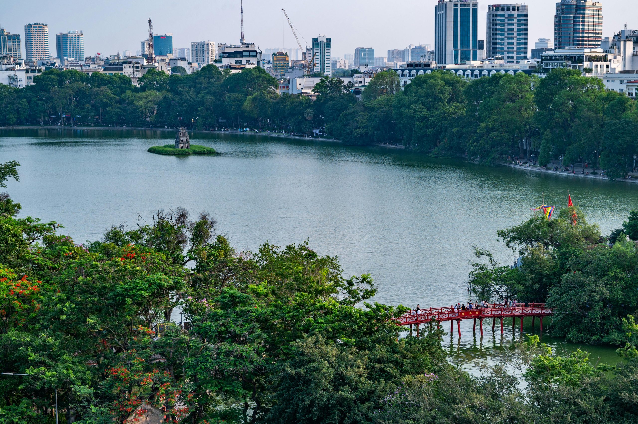 Ngoc Son Temple on Hoan Kiem Lake connected by the iconic Huc Bridge (red bridge) with traditional Vietnamese architecture and green trees
