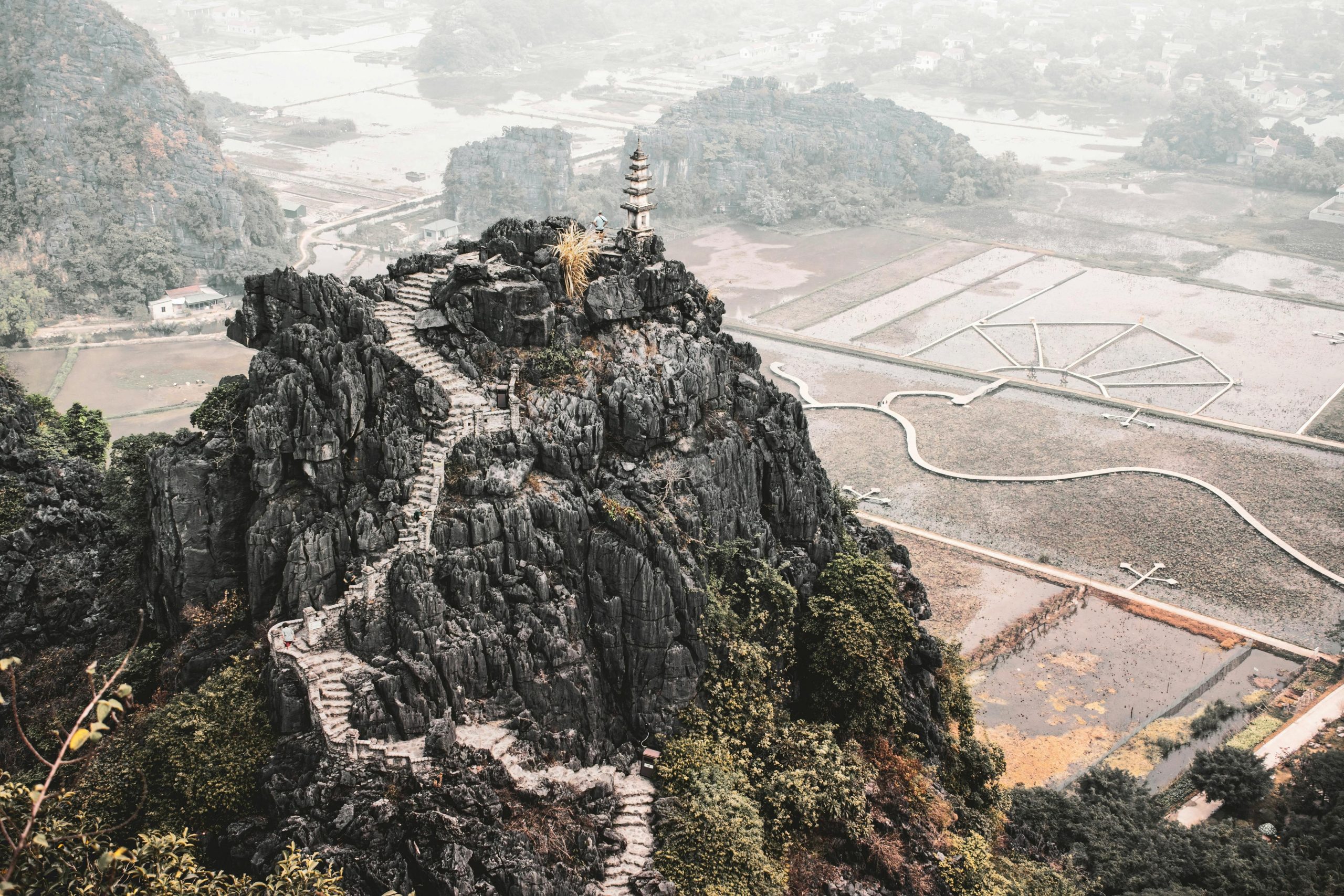 Panoramic view from the top of Mua Cave (Hang Múa) viewpoint at sunset, showing winding rivers, lush green rice paddies, and countless towering limestone karsts stretching to the horizon in Ninh Binh, with a vibrant sky.