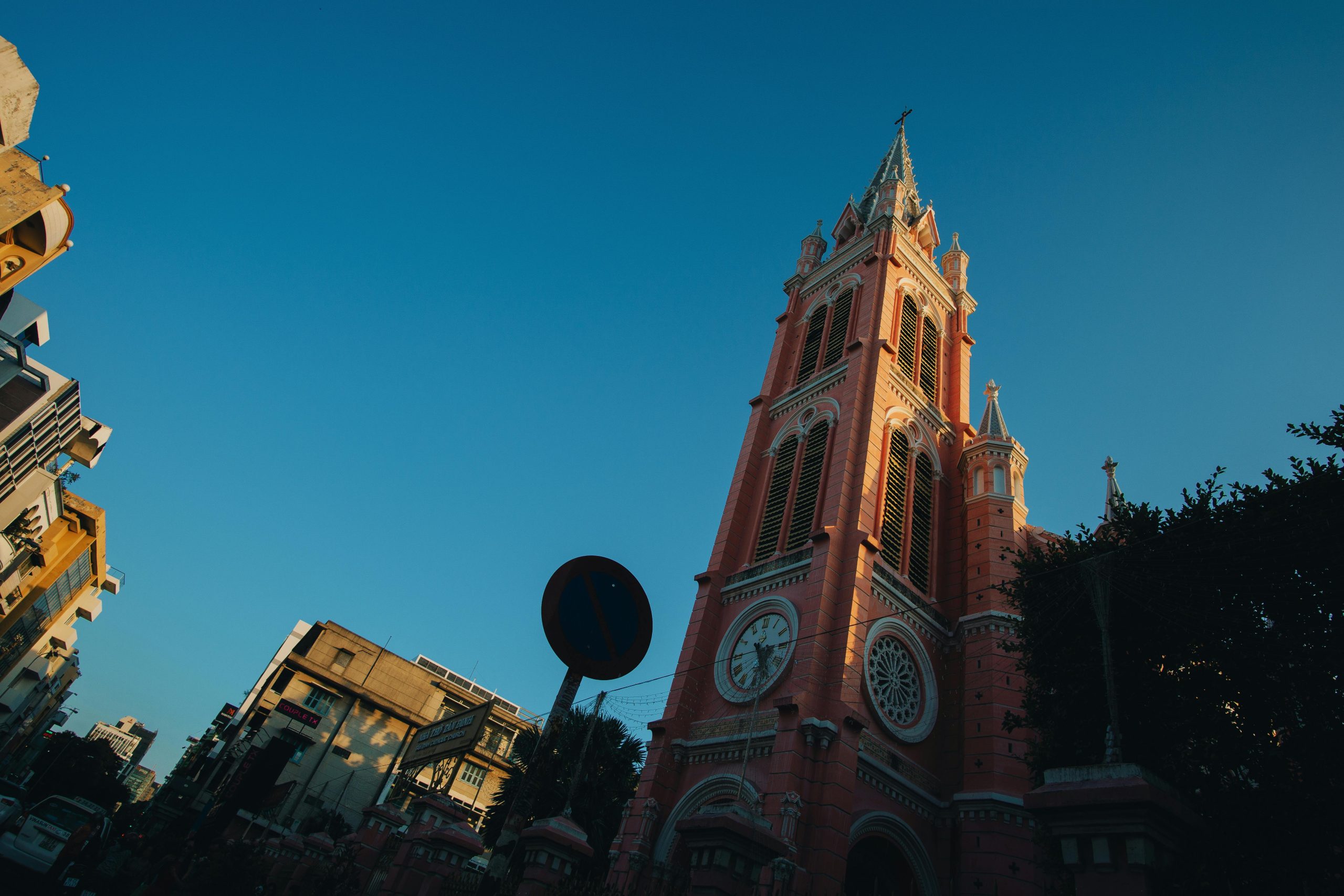 The stunning vibrant pink facade of Tan Dinh Church in District 3, Ho Chi Minh City, bathed in natural sunlight, with its tall spire reaching towards a clear blue sky and intricate architectural details visible.