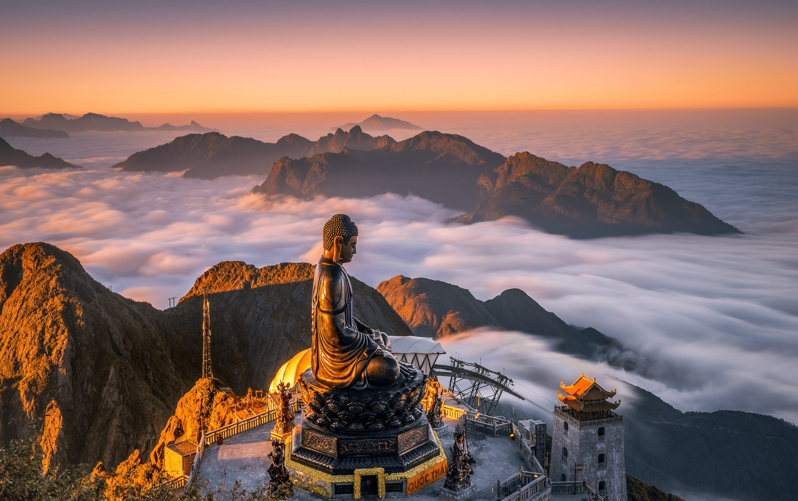 The towering bronze Great Buddha statue at Fansipan Peak summit, partially obscured by swirling mist and surrounded by traditional Vietnamese pagoda architecture